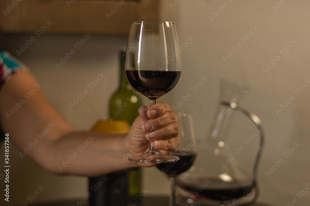 woman hand holding a wine glass over a wood table with bottle, wine container and a old lamp