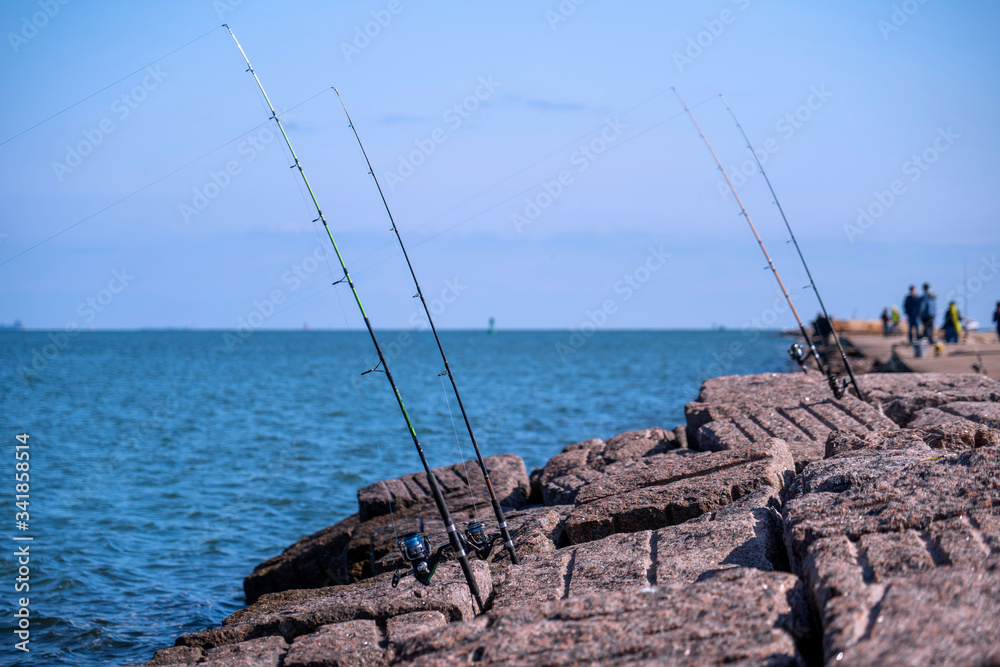 Φωτογραφία Fishing rods and reels in Port Aransas, Texas on popular jetty at the Gulf of Mexico with waves on the water