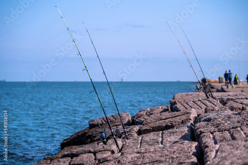 Fishing rods and reels in Port Aransas, Texas on popular jetty at the Gulf of Mexico with waves on the water.