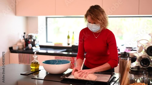 Young millennial woman cooking and rolling out the dough wearing surgical mask