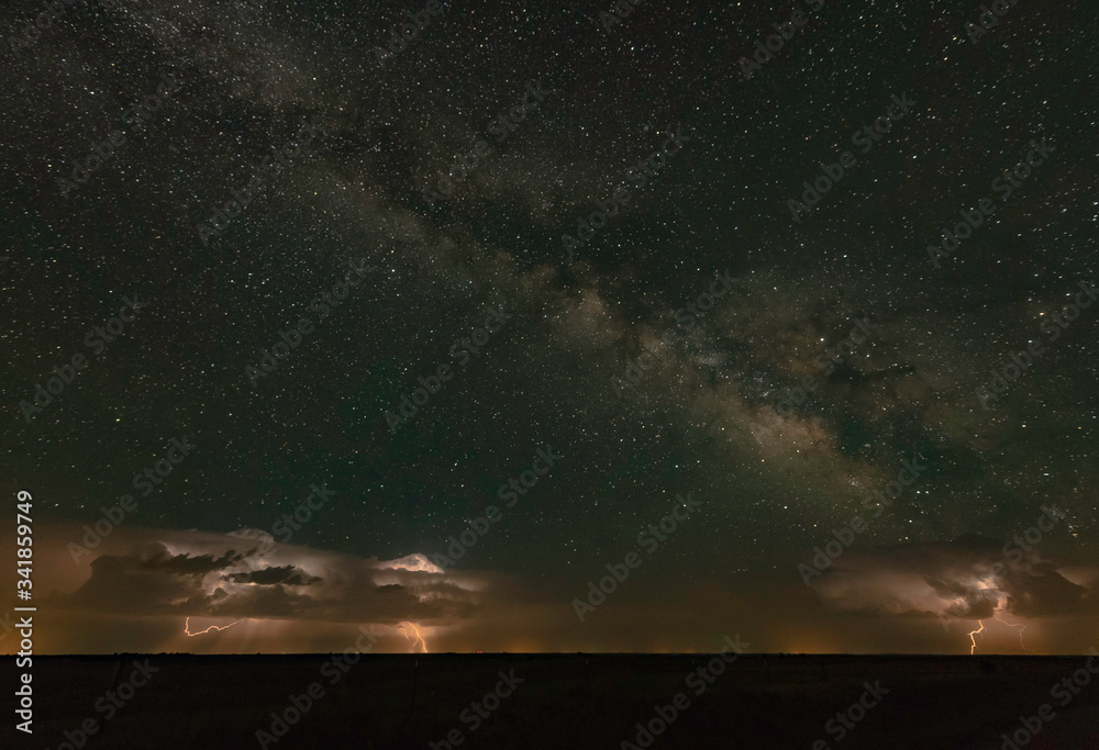Fototapeta premium A distant supercell thunderstorm is throwing lightning bolts with the milky way overhead.
