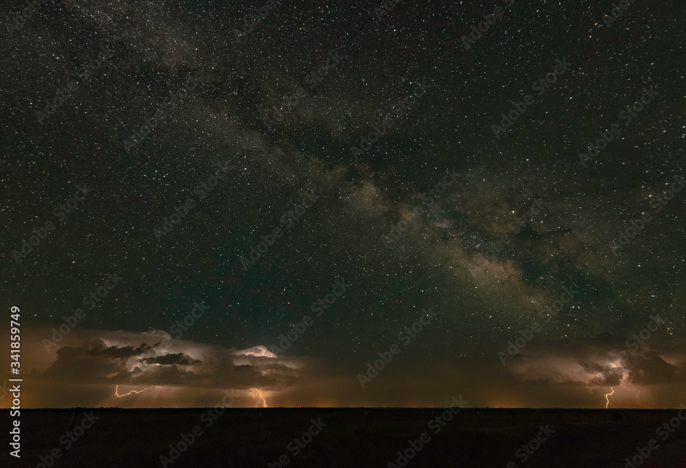 A distant supercell thunderstorm is throwing lightning bolts with the milky way overhead.