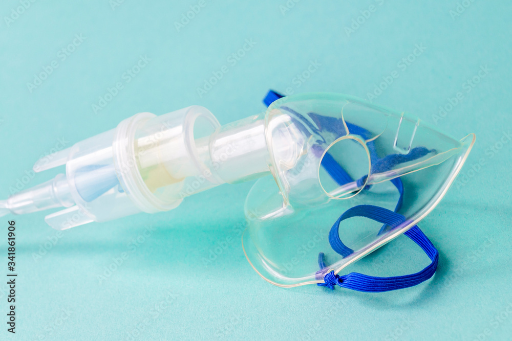 Transparent mask from an inhaler on a blue background. The device for inhalation of therapeutic steam. Transparent mask from an inhaler on a blue background. The device for inhalation of therapeutic steam.
