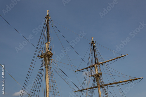 Two masts, rigging and shrouds on an old tall ship against a blue sky, horizontal aspect