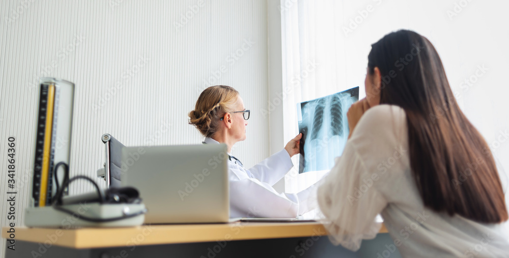 Elderly Female doctor holding and looking to young woman patient X-ray film in medical room at hospital. Elderly Female doctor holding and looking to young woman patient X-ray film in medical room at hospital.
