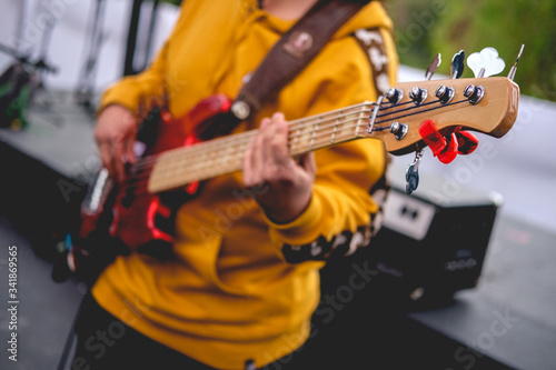 Bassist with red bass and tuner, and yellow sweatshirt playing live