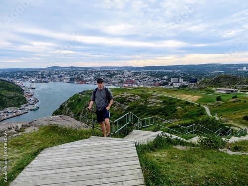 A young male tourist walking up signal hill towards cabot tower.  A famous landmark in St. Johns, Newfoundland, Canada.  St. Johns harbour is in the background.