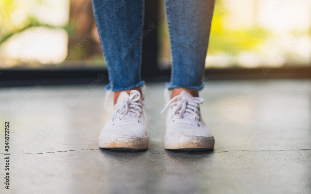 Closeup image of a woman wearing jean and white sneakers standing on concrete floor