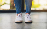 Closeup image of a woman wearing jean and white sneakers standing on concrete floor