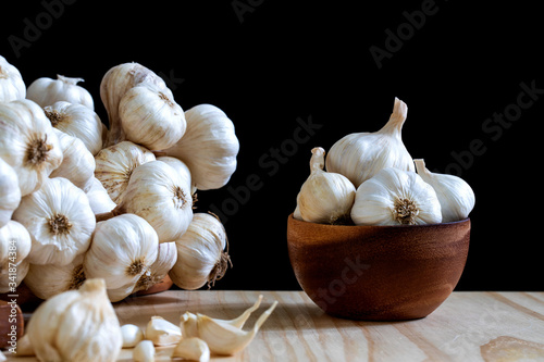 Garlic bulbs in wooden bowl and Garlic cloves on wooden table on black background..