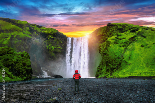Skogafoss waterfall in Iceland. Guy in red jacket looks at Skogafoss waterfall.