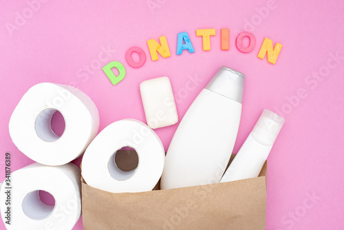 Food donation for the needy on a pink background top view. White toilet paper and hygiene products