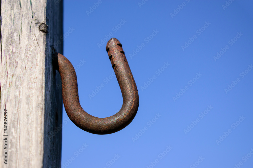 Metal hook in a wooden wall. Background is blue sky. Rusty metal, notches. Profile view.
