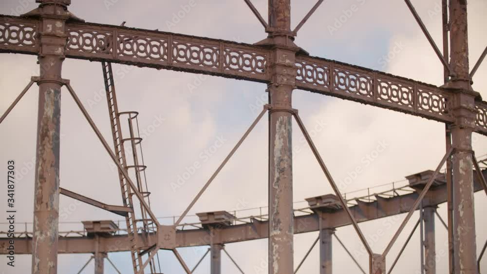 Time lapse of passing weather and clouds showing light change behind a close up rusting Victorian gas holder at gasworks in urban East London made of iron girders Time lapse of passing weather and clouds showing light change behind a close up rusting Victorian gas holder at gasworks in urban East London made of iron girders