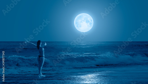 Fototapeta Naklejka Na Ścianę i Meble -  Night sky with moon in the clouds on the foreground power sea wave - Happy slim girl in red and black bikini  with raised up arms on the seashore in Alanya 