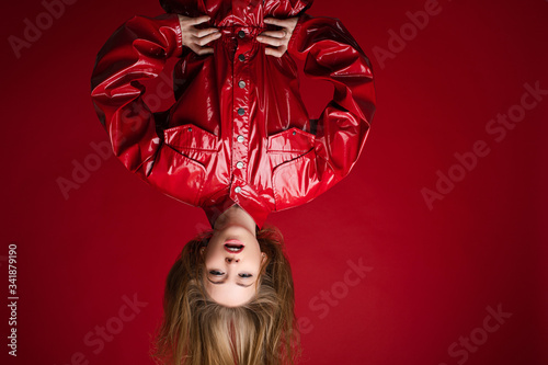 Photos Sexy fashionable girl in red leather overall hanging upside down on red background