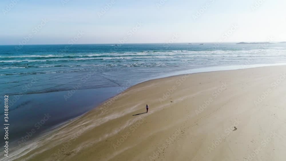 High panoramic aerial view of waves crashing onto beach, summer day on coast, woman walking along beach. West Coast, Tofino, Vancouver island, Canada. High panoramic aerial view of waves crashing onto beach, summer day on coast, woman walking along beach. West Coast, Tofino, Vancouver island, Canada.