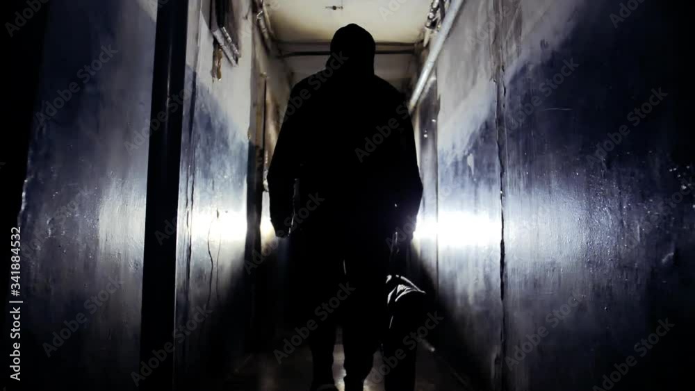 Unrecognizable Man Burglar Wearing Black Jacket and Carrying a Bag Walking Away From the Camera Along Corridor in Old Apartment Building Criminal Concept
