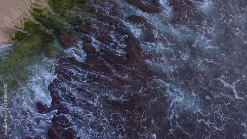 Aerial lock down view: Above the ocean, waves and water surface above coast line