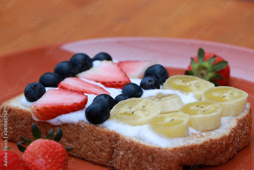 Breakfast in the round plate on the wooden floor. Slice of bread with whipped cream and fruit, Strawberry, Blueberry and Banana.