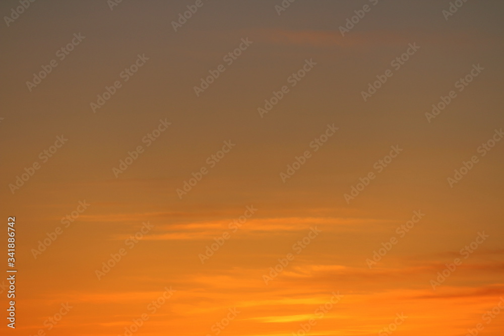 Fototapeta premium Sun below the horizon and clouds in the fiery dramatic orange sky at sunset or dawn backlit by the sun. Place for text and design.
