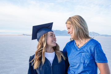 Cute Young woman in her graduation cap and gown celebrating with her mom. Beautiful girl smiling and hugging her parent after finishing her degree