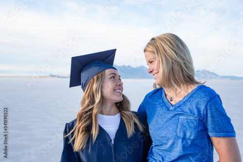 Cute Young woman in her graduation cap and gown celebrating with her mom. Beautiful girl smiling and hugging her parent after finishing her degree photo