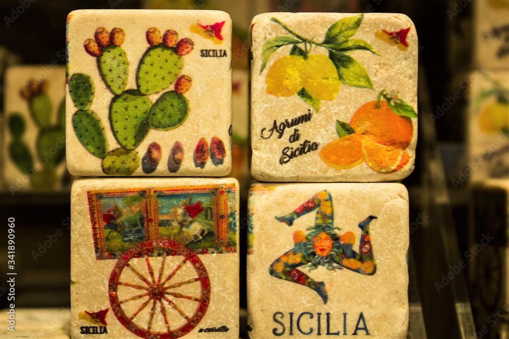 Obraz premium colored images reproduced on cube-shaped stones promoting the Sicily region in Italy depicting citrus fruits, lemons, oranges, cactuses typical Sicilian cart and female head with three folded legs c