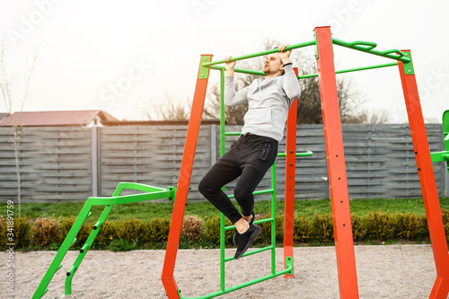 Outdoors workout. An athletic young man is doing pull-ups on the horizontal bar. Healthy lifestyle concept