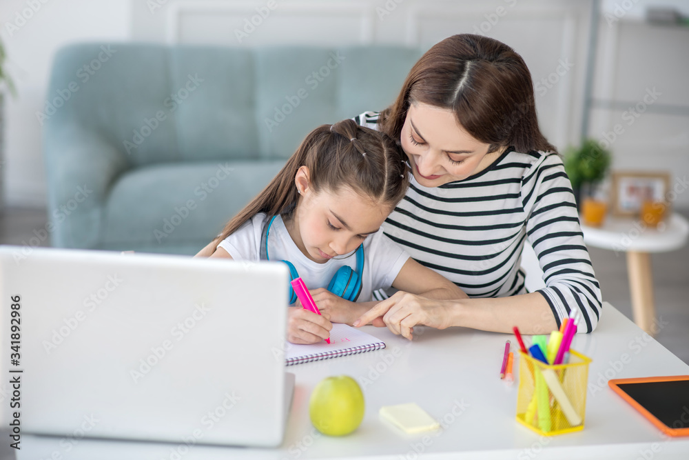 Mom with daughter are drawing at table at home.