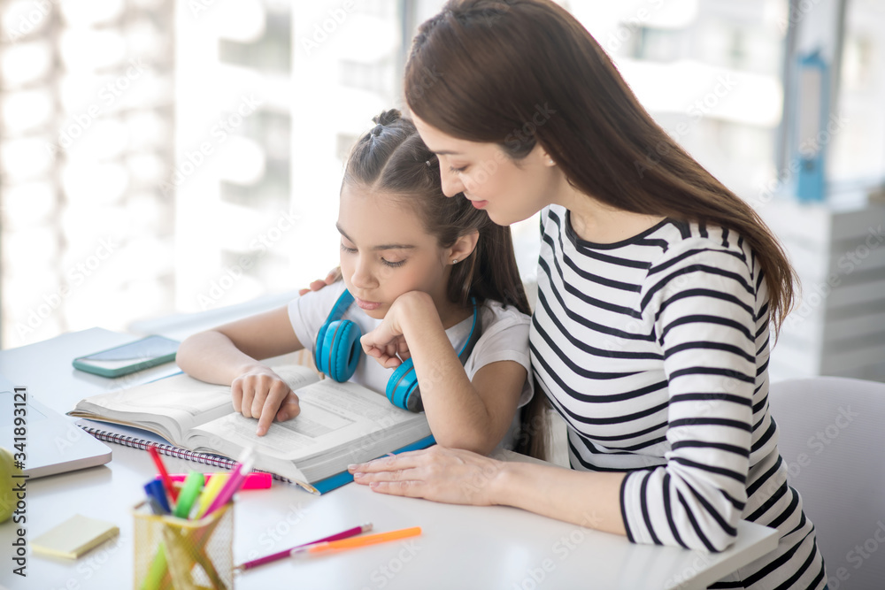 School age daughter reading a textbook with mom.