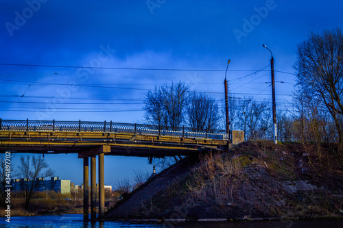 The horizontal photo shows an image of an urban area: trees, part of a bridge, and two lanterns. A quiet April evening photo