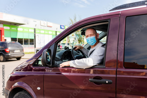 A man in a protective mask driving a car. Portrait of a man in a car in a surgical mask. A man goes to rest in the countryside.