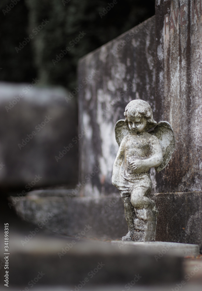 Small sculpture of a baby angel with wings on a stone grave tombstone. Old dirty worn over time