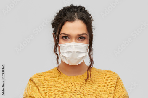 health protection, safety and pandemic concept - portrait of young woman in protective medical face mask over grey background © Syda Productions