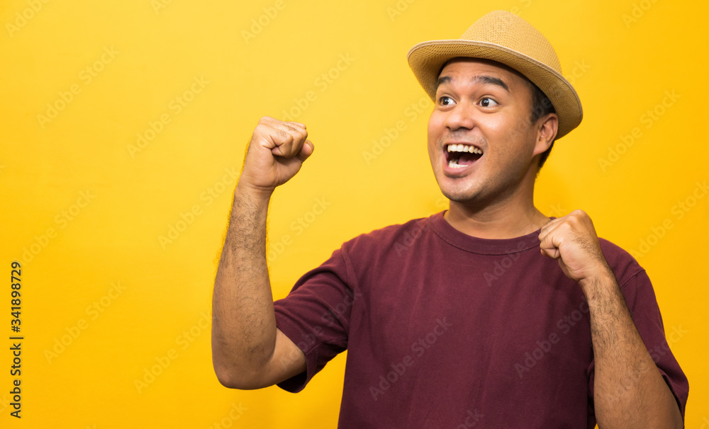 Happy young asian man celebrates with two hand in the air on yellow background. Happy young asian man celebrates with two hand in the air on yellow background.