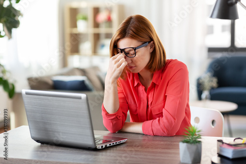 remote job, technology and people concept - tired young woman in glasses with laptop computer working and rubbing her nose bridge at home office © Syda Productions
