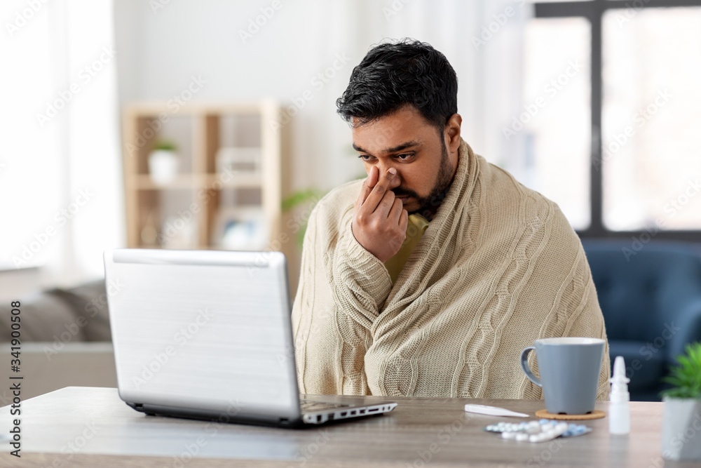 healthcare, technology and people concept - sick indian man in blanket with runny nose having video call on laptop computer at home - obrazy, fototapety, plakaty 
