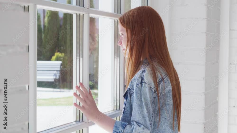Teenager girl looks out window with curiosity Teenager girl looks out window with curiosity