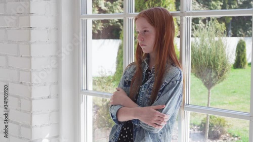 Lonely sad girl standing by window