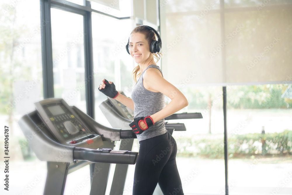Fototapeta premium Pretty young sport woman is running on treadmill in gym, Healthy lifestyle