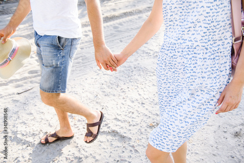 young couple in summer clothes walk on the sand holding hand