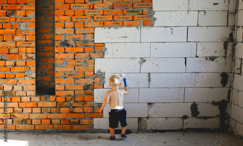 little boy in shorts at a construction site paints a wall with a paint roller