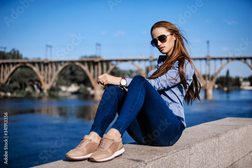 Young girl posing on the promenade on the background of the bridge in spring on a sunny day © flywish