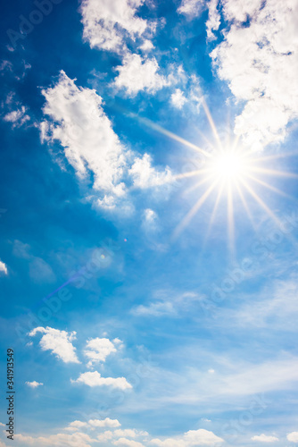 Beautiful, blue summer sky with fluffy clouds and bright sun as a background