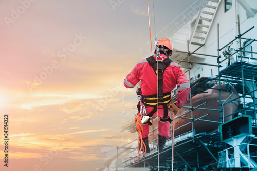 Safety first, Rope access Worker on high Abseiling of high wearing equipment protective PPE, and safety full harness for safety concept in shipyard by scaffolding background.