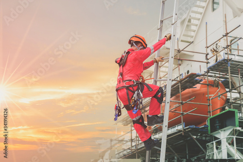 Worker on fixed ladder, Rope access Safety concept in shipyard worker wearing equipment protective full safety harness, at high places on side ship cargo ship during ship maintenance in shipyard. photo