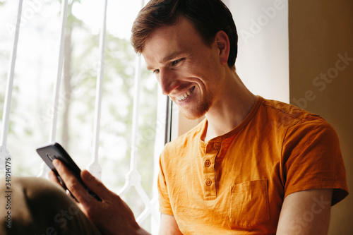 Handsome man using smartphone at home. Young man looking at his phone and smiling
