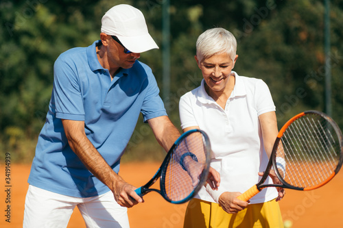 Tennis Instructor with Senior Woman on Clay Court. Woman having a Tennis Lesson. © Microgen