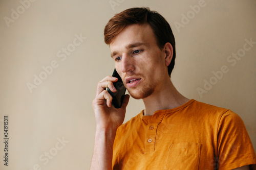 Caucasian man with beard in casual orange shirt talking with mobile phone in living room about serious problem